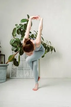 Young yogini practicing in a room with white walls and plant Stock Photos