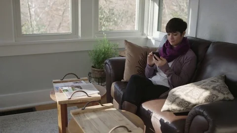 Younger lady working on a cell phone in her sunroom Stock Footage 70809616