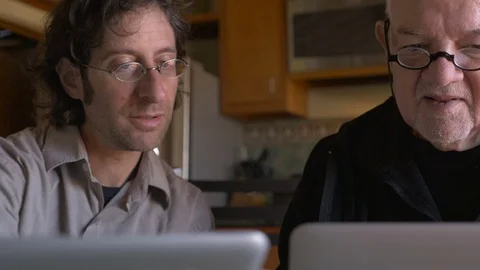 A younger man is teaching an elderly senior man how to use a laptop - dolly shot Video stock 71722998