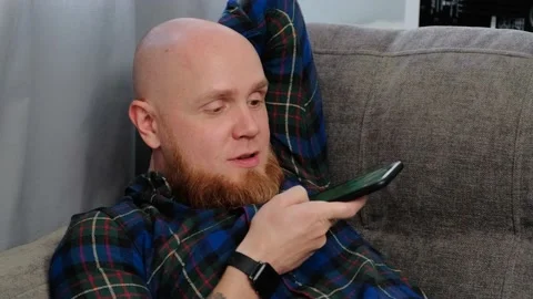 Young,white,bald man writes a voice message on a smartphone while lying on couch Stock-Footage 139647807