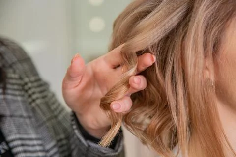In your hand to hold a lock of light brown hair curled on a curling iron Stock Photos