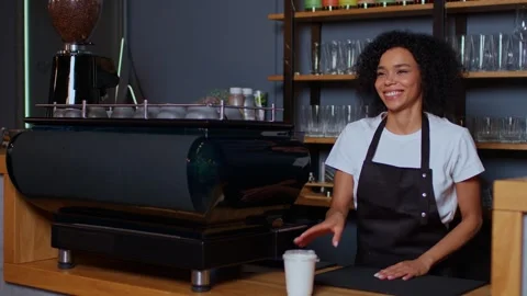 Your order is ready, a dark-skinned woman stands in a coffee shop and waves her Видео 262202853