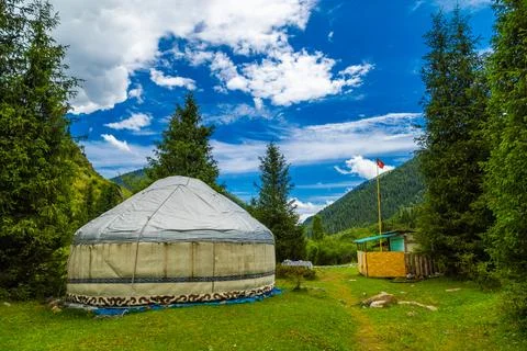 Yurt surrounded by flags, trees, and mountains in Kyrgyzstan Stockfoto's