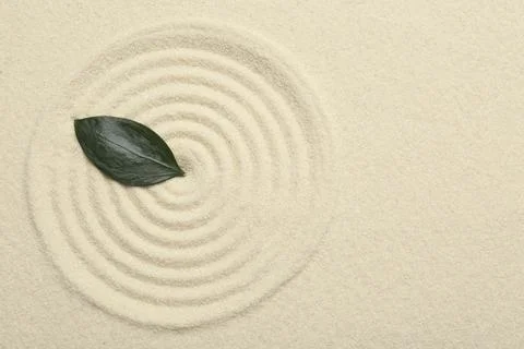 Zen rock garden. Circle pattern and green leaf on beige sand, top view Stock Photos