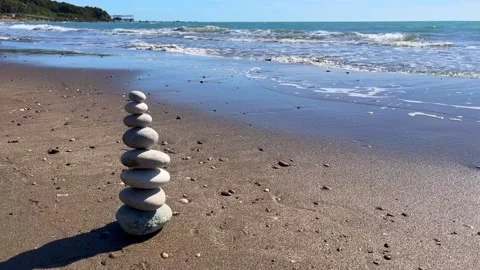 Zen stone stack on sandy beach with gentle sea waves and clear blue sky Stock Footage 310237404