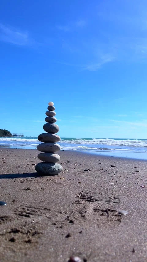Zen Stone Tower Balancing on Sandy Beach by Ocean under Blue Sky Stock Footage 310210583