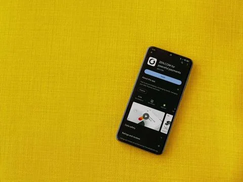 ZEN.COM app play store page on smartphone on a yellow fabric background Stock Photos