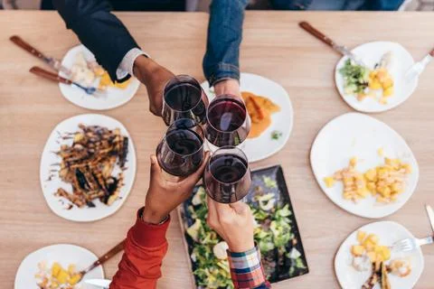 Zenith shot of 4 hands of different ethnicities toasting with red wine Stock Photos