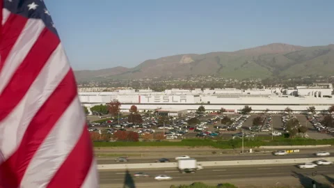 Zero emission concept. USA Flag waving by wind at Tesla Electric vehicle factory 스톡 동영상 167930295