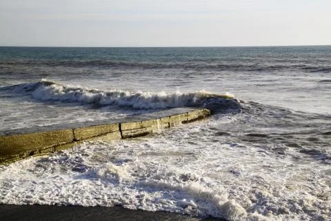Zigzag of a sea wave breaking ashore and a breakwater with sea foam Stock Photos