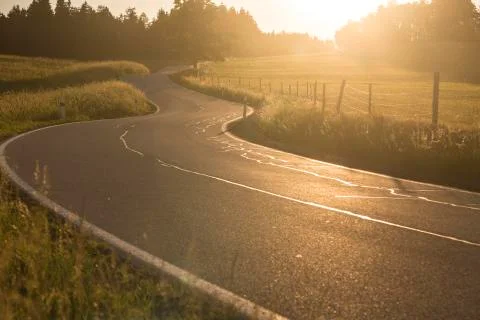 Zigzagging serpentine road between meadows just before sundown Stock Photos