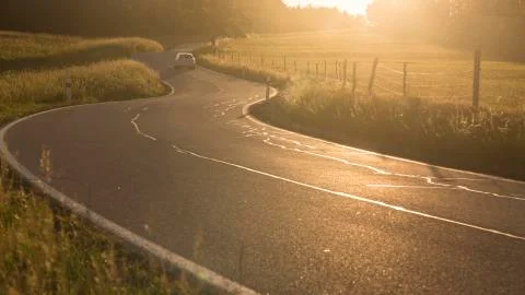 Zigzagging serpentine road between meadows just before sundown Stock Photos