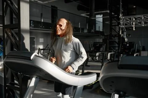 Zombie man with spooky face doing cardio workout on treadmill at gym Stock Photos