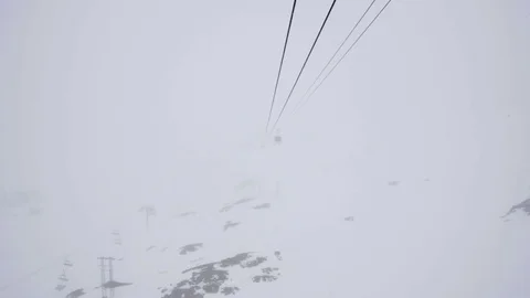 Zoom on cable car crossing deep snow covered valleys advancing through thick Stock Footage 71756601