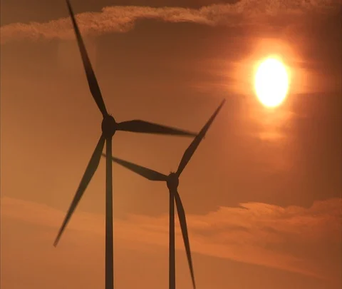 Zoom into focus, and out of focus, slowly turning wind turbines and sun. Stock Footage 86743200