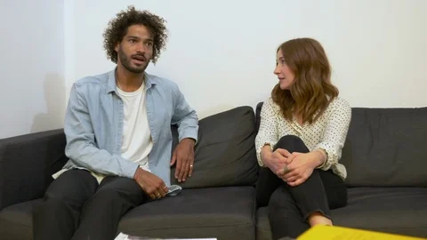 Zoom in handheld shot of young man and woman talking while sitting on sofa 스톡 동영상 114872069