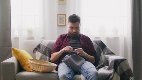 Zoom in of man sitting on couch and knitting at home Video stock 107348913