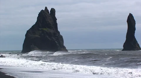 Zoom out on a breaking wave in black beach with seastack pinnacles Stock Footage 37686050