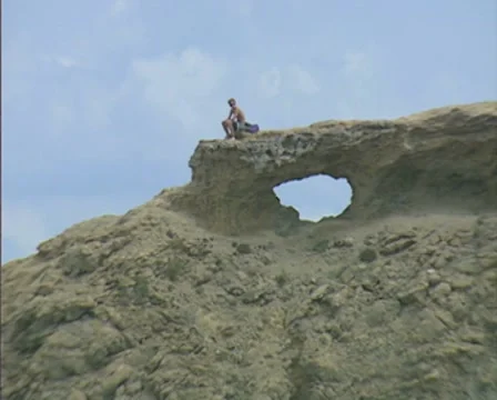 Zoom out from man sitting on top of rocky headland Video stock 8360697