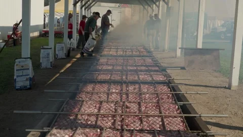 Zoom out over large open flame pit barbeque with hundreds of pork chops Stock Footage 240121686