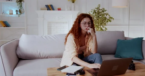 Zoom out shot of nice thoughtful woman with red curly hair sitting on sofa Video stock 138227900