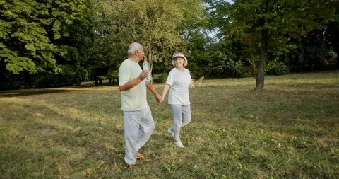 Zoom out tracking shot of elderly couple in sportswear holding hands and talking Stock Footage 129680454