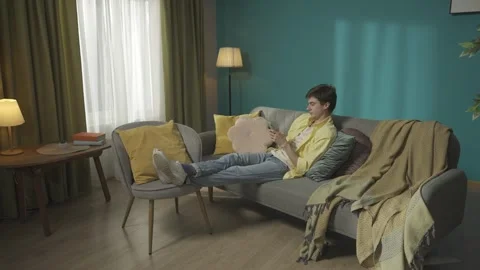 Zoom out video capturing a dark-haired man sitting on the couch, taking selfies Stock Footage 252391584