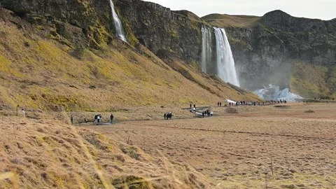 Zoom out view tourist groups visit Seljalandsfoss waterfall in Iceland in s.. Stock Footage 249822969