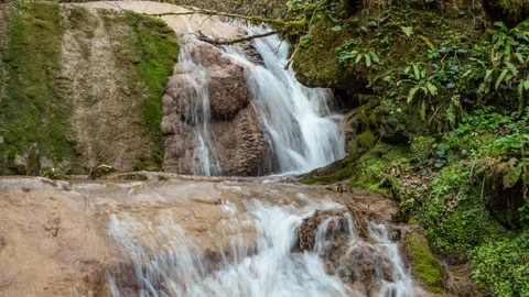 Zoom out view of a waterfall surrounded by moss-covered rocks in a green fore Stock Footage 150677134