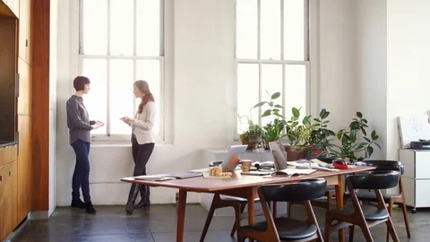 Zoom in shot of businesswomen talking while standing by window in creative Stock Footage