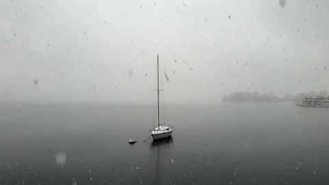 Zoom in shot of snow falling over lake maggiore and moored sailing boat Stock Footage 279907326