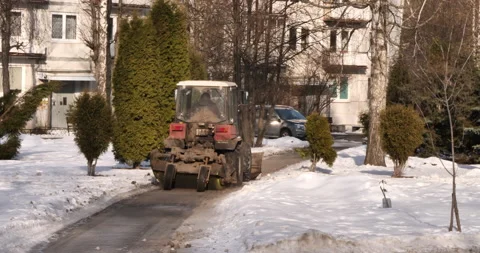 Zoom in small red tractor drives on the sidewalk and shovels snow near buildings Stock Footage 238772868