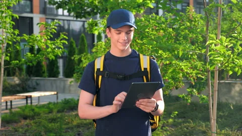 Zoom in smiling man courier food delivery with thermal backpack uses tablet Stock Footage 157446417
