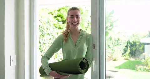 Zoom spurring woman stepping through glass door holding yoga mat, adjusting Stock Footage 340986831