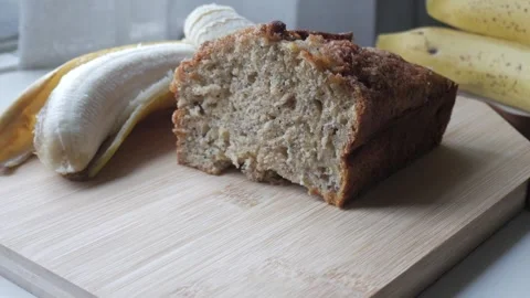 Zoom in view of banana bread cut in half on a wooden board with a banana in the 스톡 동영상 296574745
