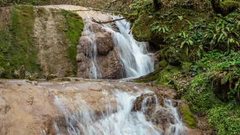 Zoom in view of a waterfall surrounded by moss-covered stones in a green fore Stock Footage 150550750