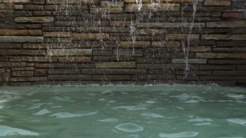 Zoom in water falling down stone wall into pool Stock Footage 76256549