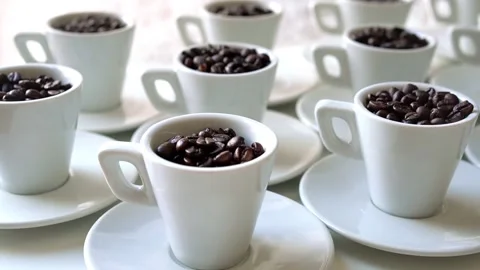 Zoom in on a white coffee cups filled with coffee beans arranged on a white tabl Stock Footage 281791771