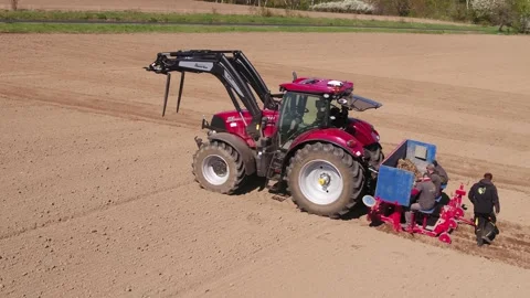 Zoom in on workers loading machine attached to red tractor on farm field Stock Footage 313096432