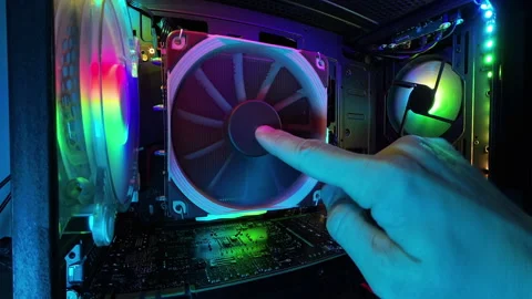 A zoomed-in view inside a gaming PC, featuring a hand stopping the RGB-lit Stock Footage 289764745