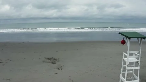 Zooming in on a deserted beach with small waves alongside a lifeguard post Stock Footage 146345096