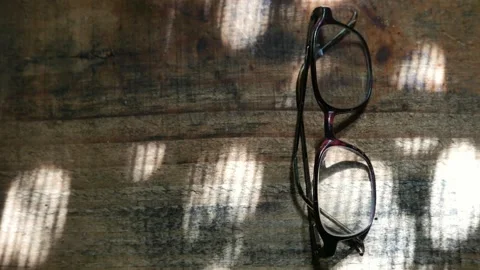 Zooming in: intense sunbeams moving over a pair of old glasses on the table Stock Footage 277018792