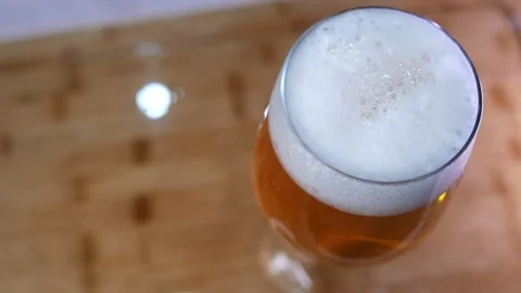 Zooming out from a beer glass on the table. Bubbles bursting in beer foam Stock Footage 332391899