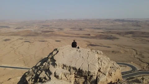 Zooming out on a guy sitting on crater's edge in the middle of the desert at the Stock Footage 152033795
