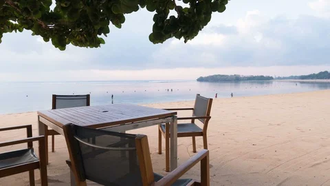 Zooming out timelapse of table and chairs under a tree on beach in morning. Bali Stock Footage 111227038