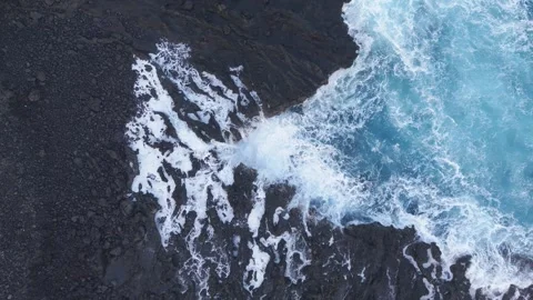 Zooming out on turquoise waves pounding volcanic rocks, exposing dramatic Stock-Footage 308420610