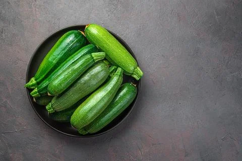 Zucchini in a black plate on a gray-brown background. Stock Photos