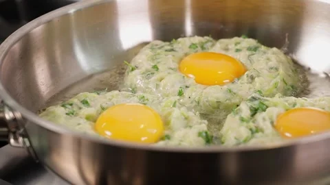 Zucchini pancakes with an egg in the middle are fried in a metal frying pan Stock Footage 270150455