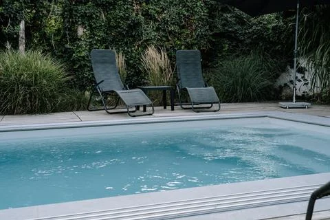 Zwei Liegesthle an einem Pool und einem grnen Garten im Hintergrund. Urlaub Stock Photos